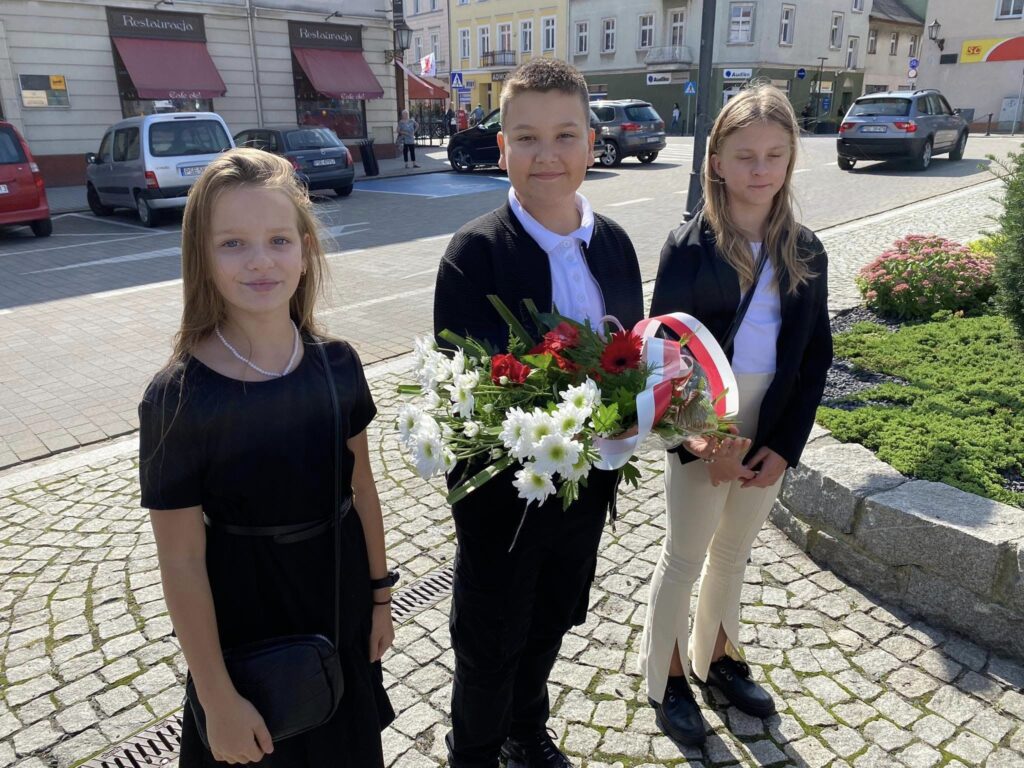 Uczniowie stoją z kwiatami.