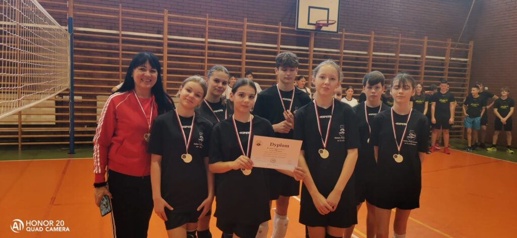Uczniowie stoją z medalami na sali gimnastycznej